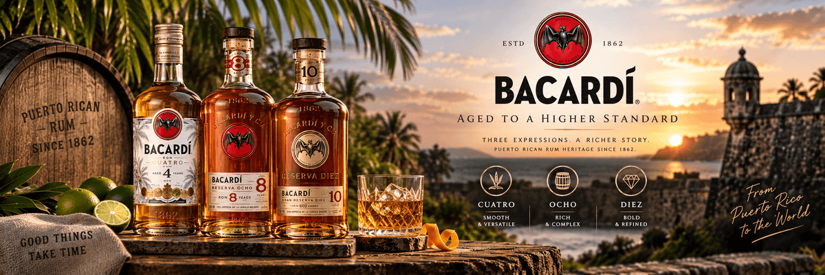 Bacardi Aged to a Higher Standard whiskey bottles displayed on a wooden crate beside a barrel, with a glass of amber liquor and citrus slices in the foreground. The background shows a sunset over a tropical island scene with palm trees and a historic stone building.